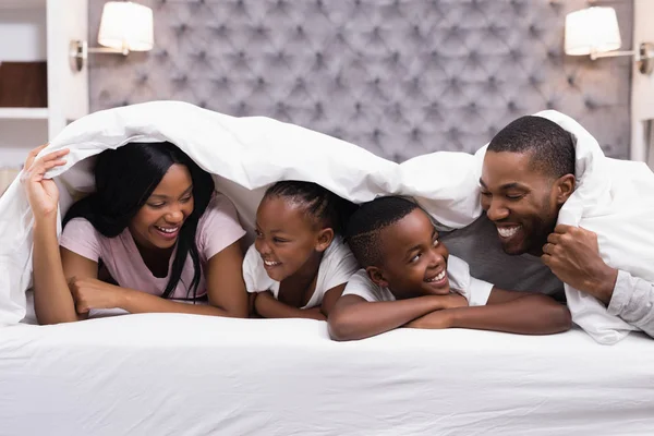 Family lying together under blanket on bed — Stock Photo, Image