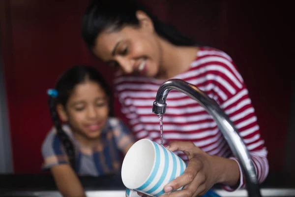 Mujer con hija lavado taza en el fregadero —  Fotos de Stock