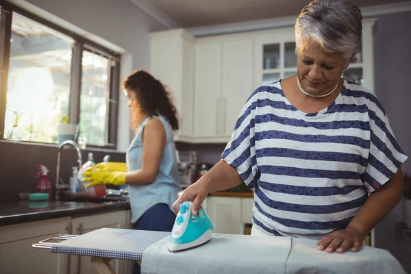 Madre planchando ropa mientras su hija lava utensilios —  Fotos de Stock