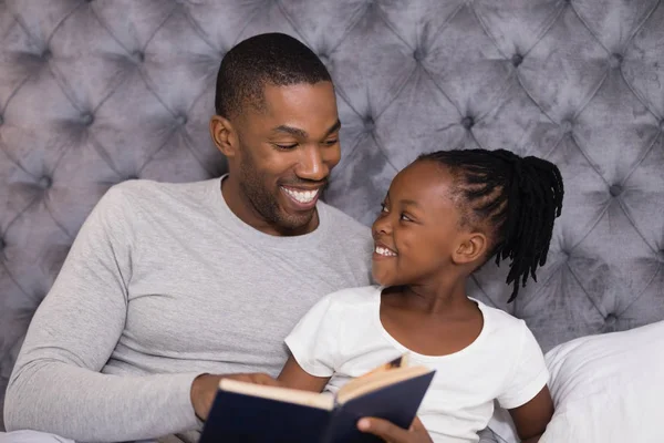 Man met dochter leesboek op bed — Stockfoto