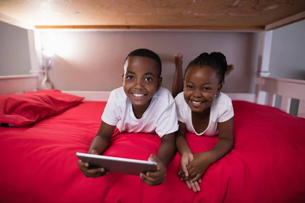 Frères et sœurs avec tablette couchée sur le lit à la maison — Photo
