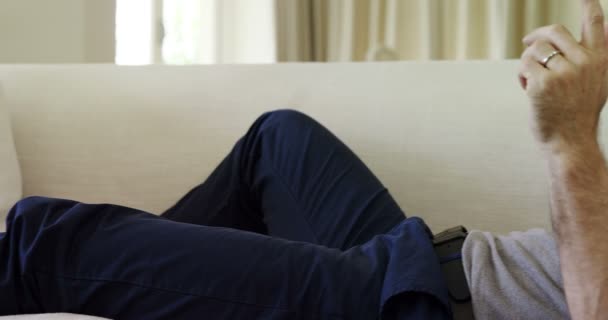 Зрелый мужчина разговаривает по телефону, лежа на диване — стоковое видео