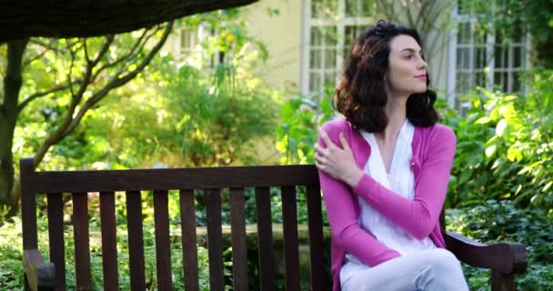Vrouw zitten op bankje in tuin — Stockvideo