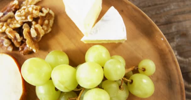 Queso con uvas, rodajas de manzana, nueces y salsa en plato de madera — Vídeos de Stock