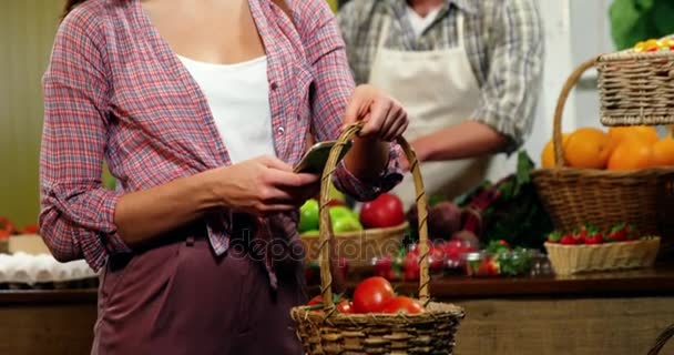Kvinna med mobiltelefon samtidigt köper tomater — Stockvideo