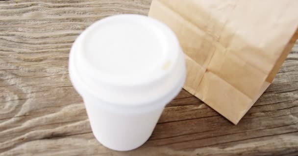 Disposable coffee cup and parcel on wooden plank — Stock Video