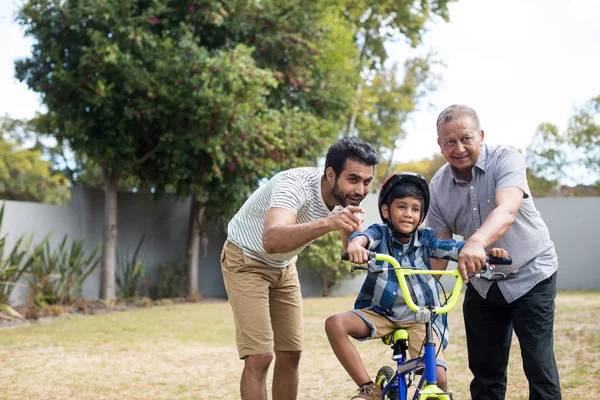 Menino aprendendo bicicleta com pai e avô — Fotografia de Stock
