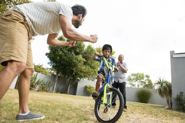 Vader en grootvader juichen voor jongen fietsen — Stockfoto