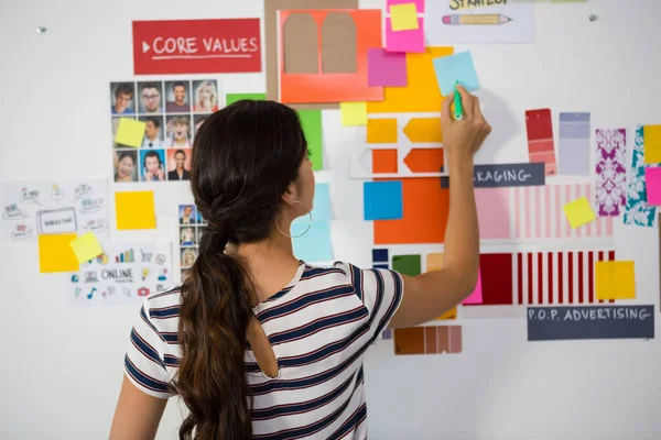 woman writing on sticky note in office