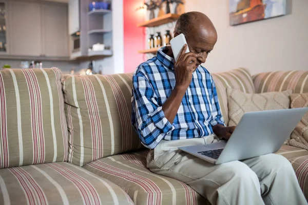 Hombre hablando por teléfono mientras usa el ordenador portátil — Foto de Stock