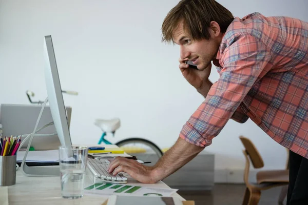 Homem falando no telefone ao usar o computador — Fotografia de Stock