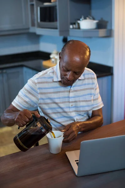 Człowiek wylewanie kawy siedząc przy laptopie — Zdjęcie stockowe