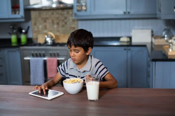 Menino usando tablet enquanto toma café da manhã — Fotografia de Stock