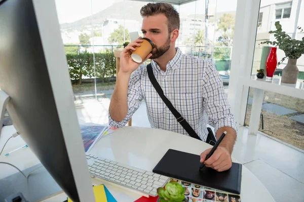 Designer having drink writing on graphics tablet — Stock Photo, Image