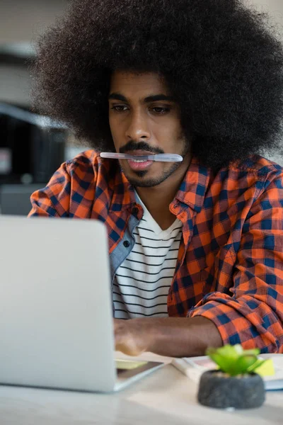 Homem com caneta na boca usando laptop — Fotografia de Stock