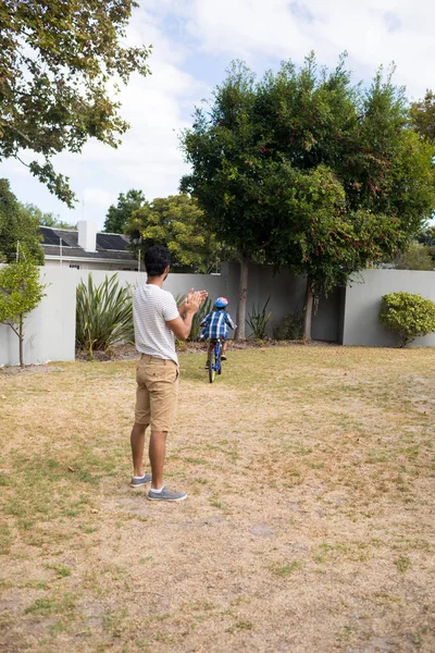 Padre aplaudiendo mientras hijo ciclismo en el patio — Foto de Stock