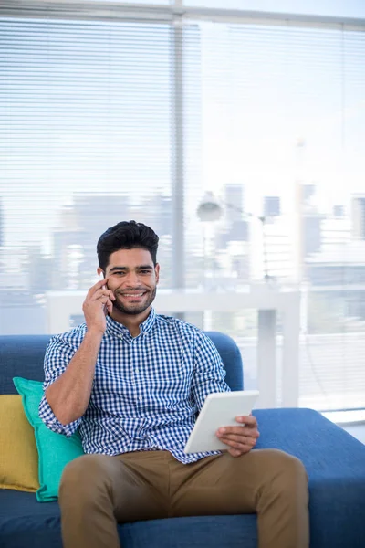 Executivo masculino usando tablet falando no telefone — Fotografia de Stock