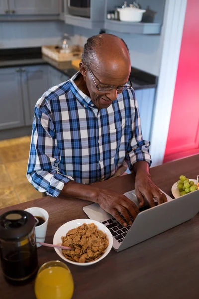 Starszy człowiek korzysta z laptopa w kuchni — Zdjęcie stockowe