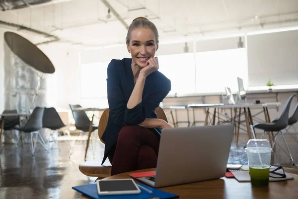 Businesswoman with hand on chin sitting in office — Stock Photo, Image