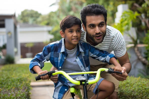 Отец смотрит в сторону, помогая сыну на велосипеде — стоковое фото