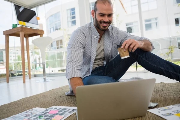 Designer holding disposable cup using laptop — Stock Photo, Image