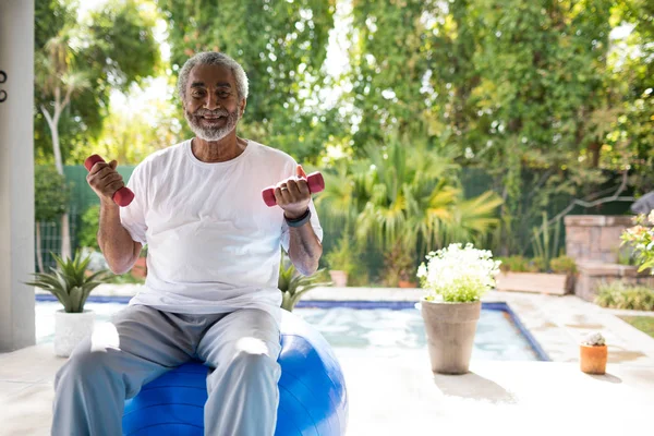 Homem segurando halteres na bola de fitness — Fotografia de Stock