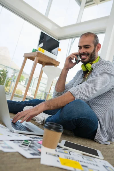 Designer talking on phone while using laptop — Stock Photo, Image