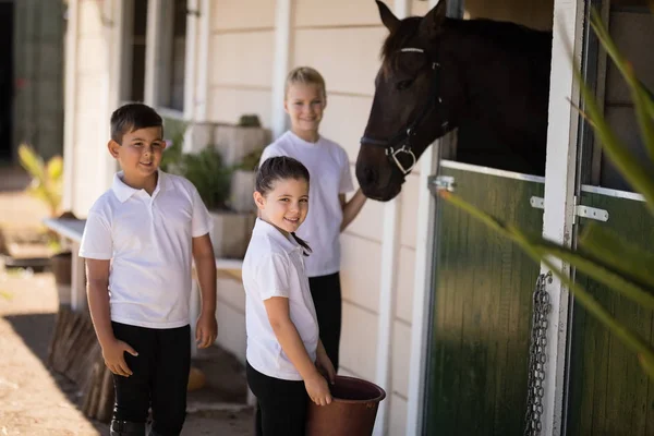 Niños sonrientes alimentando al caballo en establo — Foto de Stock