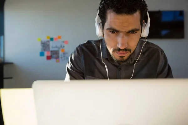 Affärsman som lyssnar på hörlurar medan du använder laptop — Stockfoto