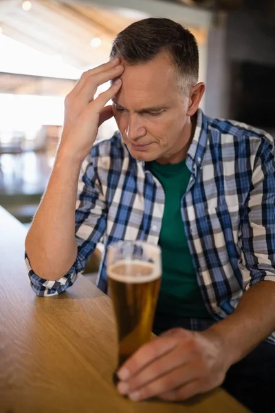 Orolig man sitter på bar med glas öl — Stockfoto