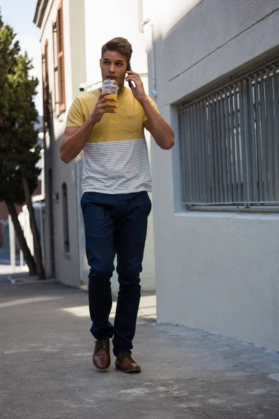 Чоловік п'є сік під час розмови на смартфоні — стокове фото
