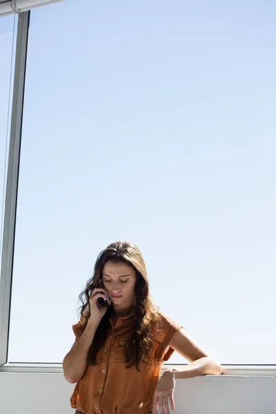 Businesswoman talking on mobile phone by window — Stock Photo, Image