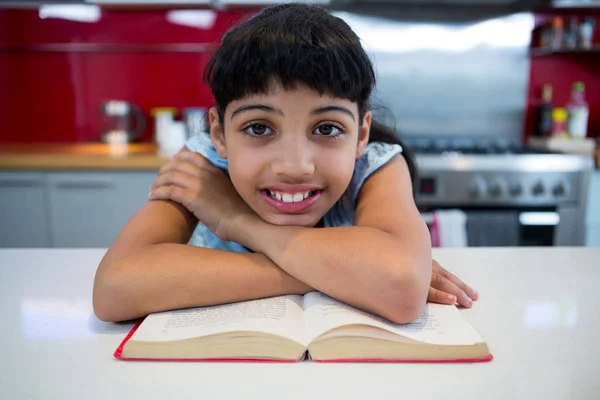 Chica sonriente sentada con libro en la cocina —  Fotos de Stock