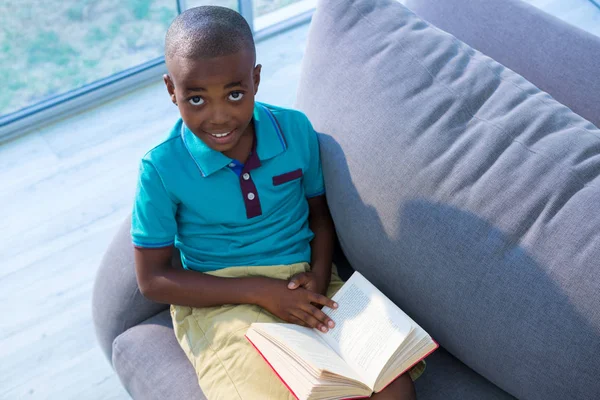 Niño sentado con libro en sofá Fotos de stock