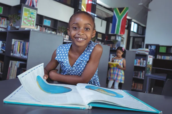 Flicka med boken på skrivbord i biblioteket — Stockfoto