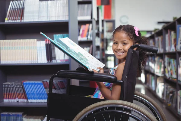 Menina sorridente com livro em cadeira de rodas — Fotografia de Stock