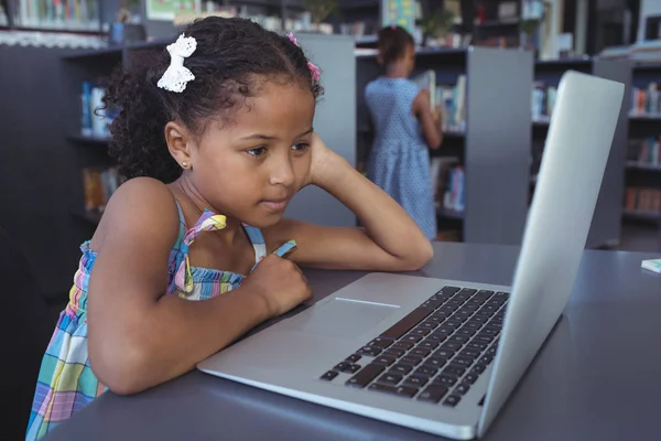 Menina concentrada olhando para laptop na biblioteca — Fotografia de Stock