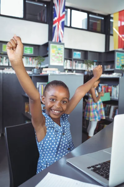 Девушка с поднятыми руками за столом в библиотеке — стоковое фото