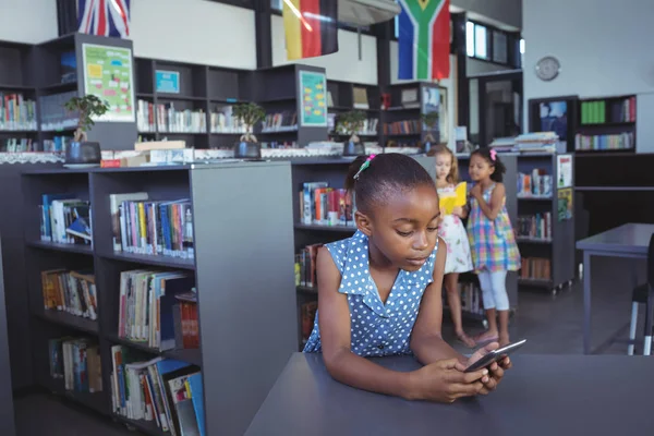 Meisje met behulp van mobiele telefoon op Bureau in bibliotheek — Stockfoto