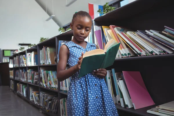 Mädchen liest Buch im Bücherregal in Bibliothek — Stockfoto