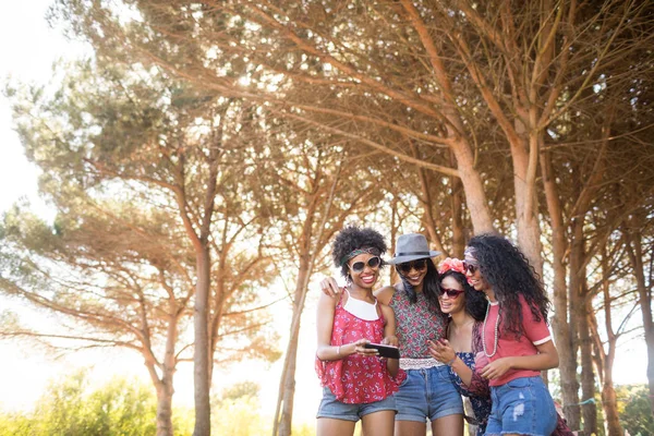 Amici di sesso femminile utilizzando il telefono cellulare contro gli alberi — Foto Stock