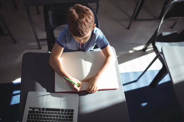 Jongen in boek schrijven door laptop aan balie — Stockfoto