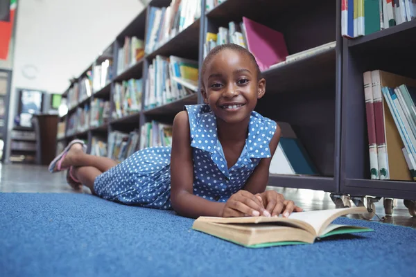 Χαμογελαστό κορίτσι με το βιβλίο που βρίσκεται από το ράφι βιβλιοθήκης — Φωτογραφία Αρχείου