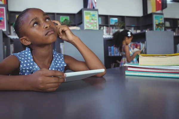 Menina pensativo segurando tablet digital na biblioteca — Fotografia de Stock