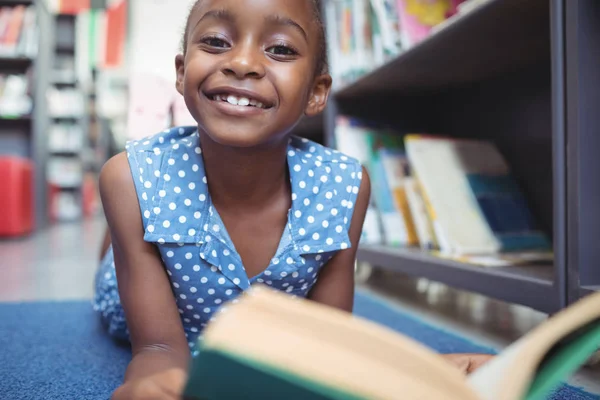 Lachende meisje met boek in bibliotheek — Stockfoto