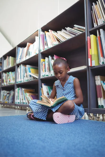 Menina lendo livro enquanto sentado na biblioteca — Fotografia de Stock