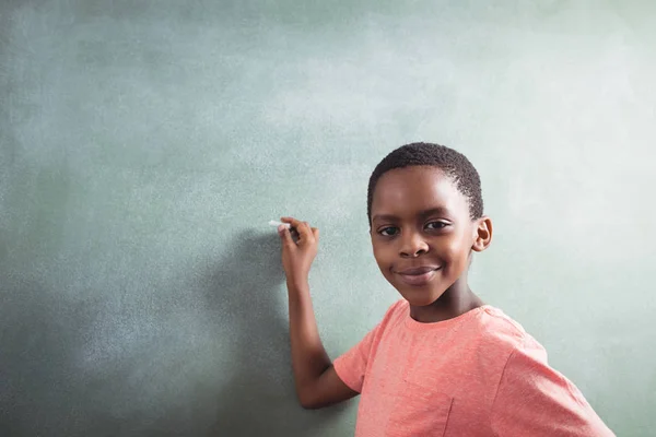 Boy standing by chalkboard — Stock Photo, Image