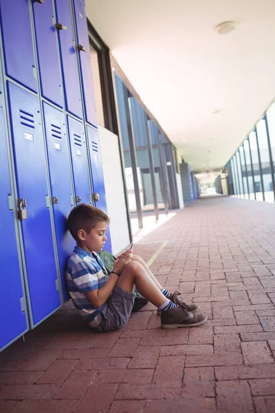 Boy using phone while sitting by lockers — Stock Photo, Image