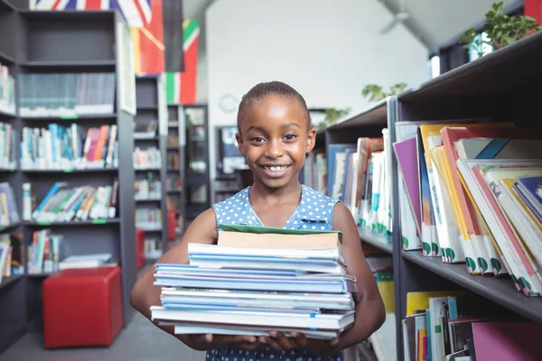 Usmívající se dívka nesoucí knihy v knihovně — Stock fotografie