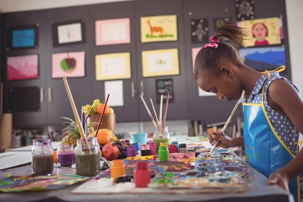Mädchen hält Pinsel nach Farbpaletten auf Schreibtisch — Stockfoto